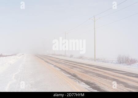 Schneebedeckte Asphaltstraße, die durch den Nebel im ländlichen Prince Edward Island, Kanada führt. Stockfoto