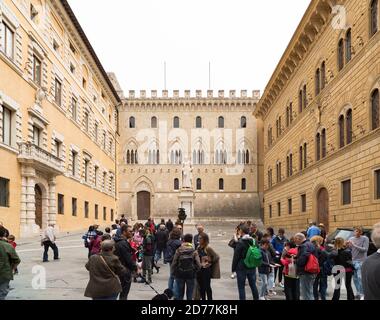 SIENA, ITALIEN - 22. APRIL 2019: Touristen auf einem der vielen Plätze der italienischen Stadt mit der Statue von sallustio bandini im Hintergrund Stockfoto