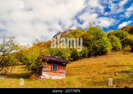 Herbstlandschaft in den Bergen. Berg Herbst Szene mit bunten Bäumen im Wald. Es gibt einige Häuser und Hütten auf der Wiese Stockfoto