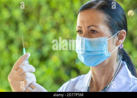 Selbstbewusste Ärztin im Krankenhausgarten mit Spritze und Gesundheitsmaske. Stockfoto