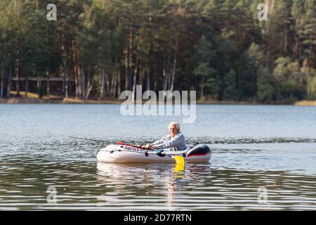 Kadaga, Lettland - 27. september 2020: Ein Fischer fischt auf Angelruten von einem Gummiboot mit Rudern, Wald auf einem verschwommenen Hintergrund Stockfoto