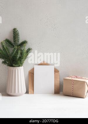 Weihnachtsbaum Zweige Vase, offene Kraftumschlag und leere Postkarte in der Nähe der grauen Wand und verpacktes Geschenk. Vorderansicht. Speicherplatz kopieren Stockfoto