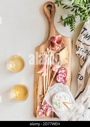Snack-Wein-Set. Vielfalt an Wurst, Oliven, Käse, Brotstäbchen, auf Holzschneidebrett und zwei Weingläser auf hellem Hintergrund. Flach liegend. Oben vi Stockfoto