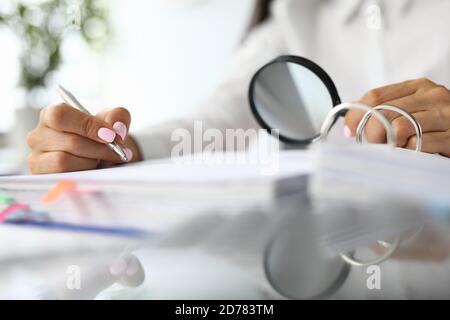 Weibliche Hände halten Lupe und Stifte neben Dokumenten. Stockfoto