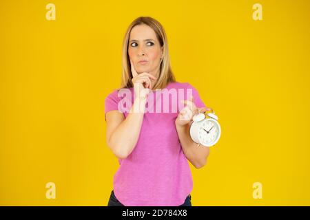 Porträt einer nachdenklichen Casual Frau mit Wecker Blick auf den über gelbem Hintergrund isolierten Kopierbereich Stockfoto