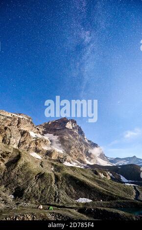 Vertikale Aufnahme des Matterhorns oder des Monte Cervino aus Italien bei Nacht, Zeltlager unter blauem Himmel mit Sternen und Milchstraße. Wunderschöne Bergrücken mit hohen felsigen Gipfeln, Wunderland. Konzept des Reisens Stockfoto