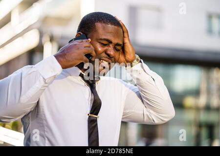 Porträt eines frustrierten afroamerikanischen Geschäftsmannes, der Smartphone benutzt. Stockfoto