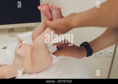 Mutter ändert die Windel eines kleinen Neugeborenen, während es auf dem Rücken auf einem Wickeltisch im Kinderzimmer liegt. Babyhygiene eine feuchte Serviette. Stockfoto