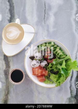 Poke eine Schüssel mit Lachs, Gemüse, Reis und Algen neben Sojasouce und Tasse Kaffee aus der oberen Ansicht. Gesundes Frühstückskonzept Stockfoto