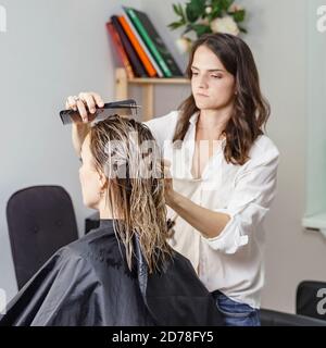 Schöne Frau Stylistin macht einen Haarschnitt zu einem blonden Kunden Stockfoto