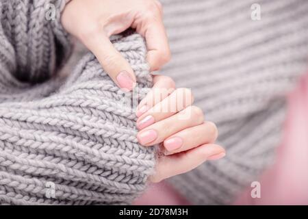 Weibliche Hände halten großen grauen Wollschal. Maniküre mit rosa Nagellack, glänzendes Design. Draufsicht Stockfoto