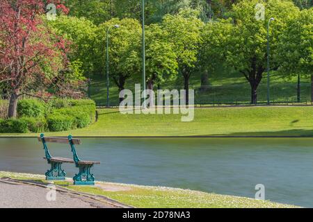 Blick auf einen kleinen Park mit einer Bank, einem Teich und der Straße mit Spuren eines Autos in Bewegung. Stockfoto