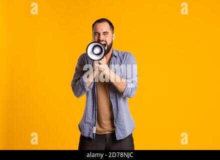 Ein bärtiger Mann in einem lässigen Hemd mit Lautsprecher In seinen Händen schreit in ein Megaphon auf einem gelben Hintergrund Stockfoto