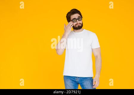 Junger bärtiger Mann in einem weißen T-Shirt mit 3D Brillen sehen ein Filmmelodrama auf gelbem Hintergrund Stockfoto