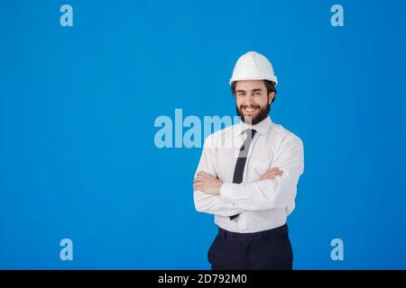 Männlicher Ingenieur Architekt in einem weißen Hemd und Bauhelm auf blauem Hintergrund, Studio Portrait. Der Bauarbeiter kreuzt seine Arme und Stockfoto