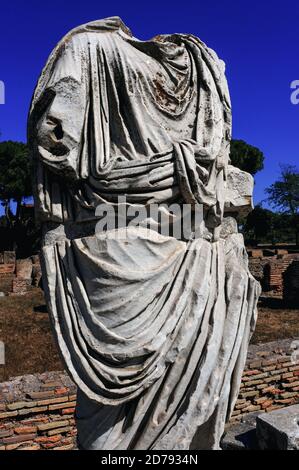 Kopflose männliche Statue in der Nekropole Porta Romana in Ostia Antica, Latium, Italien, inmitten von Familiengräbern entlang der Via Ostiensis, der Autobahn, die östlich zum antiken Rom führt. Ostia wurde im 7. Jahrhundert v. Chr. an der Mündung des Tiber als Seehafen Roms gegründet, liegt aber jetzt landeinwärts, nachdem die Verlandung den Flussverlauf geändert hatte. Sie blühte sowohl in republikanischer als auch in kaiserlicher Zeit und erreichte höchsten Wohlstand, als Kaiser Paläste, Denkmäler und öffentliche Gebäude errichteten, aber weitere Verlandungen kosteten Ostia seine Hauptrolle. Es wurde schließlich von Westgoten und Vandalen geplündert und schließlich im 9. Jahrhundert aufgegeben. Stockfoto