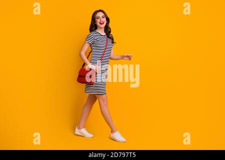 Ganzkörper-Profil-Foto von hübschen tausendjährigen Dame roten Lippen Spaziergang Straße sonniges Wetter Tag Shopping Wochenende tragen lässig gestreift Kurze Clutch Stockfoto