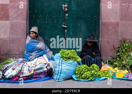 24. Februar 2020: Frauen tragen traditionelle Kleidung und verkaufen Stoffe, Blumen und Gemüse auf der Straße. Potos’, Bolivien Stockfoto