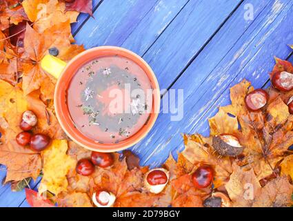 Stillleben mit einer Tasse Tee, Rosskastanien und Herbstblättern auf blauen Holzbrettern im Herbstgarten. Stockfoto