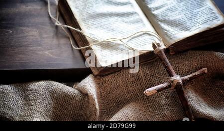 Religiöse altes Buch auf einem Holztisch. Eine religiöse Kreuz mit einem Seil und Sackleinen, neben der Bibel gebunden. Gottesdienst, Sünden und das Gebet. Stockfoto