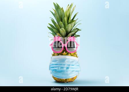 COVID Travel Konzept. Ananas in Sonnenbrille und medizinische Maske auf blauem Hintergrund. Ananas in rosa Sonnenbrille und Gesichtsmaske - Neue normale Reise Stockfoto