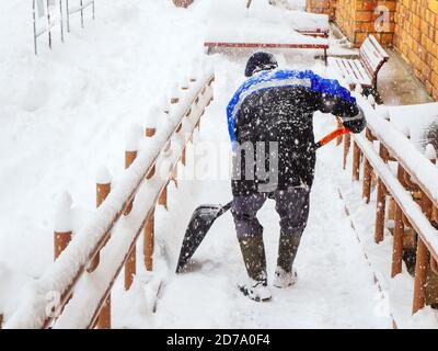 Ein Arbeiter räumt Schnee von der Veranda eines Hauses Bei starkem Schneefall Stockfoto