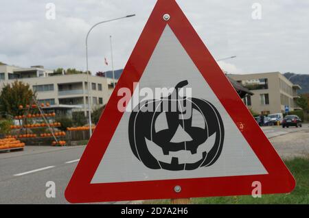 Ein Dreieck Straßenschild mit einem geschnitzten Kürbis an der Straßenseite. Im Hintergrund ein Hofladen mit Produkten einer lokalen Kürbisfarm für Halloween. Stockfoto