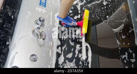 Reinigung der Duschdampfkabinen von Kalziumablagerungen. Reinigung im Badezimmer. Hand in Handschuhe mit Lappen und Waschmittel Dusche und Glas waschen Stockfoto