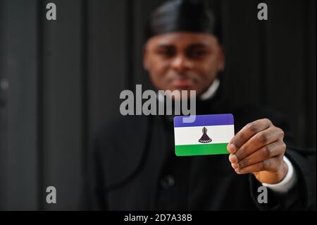 Afrikanischer Mann tragen schwarz durag halten Lesotho Flagge bei der Hand isoliert dunklen Hintergrund. Stockfoto