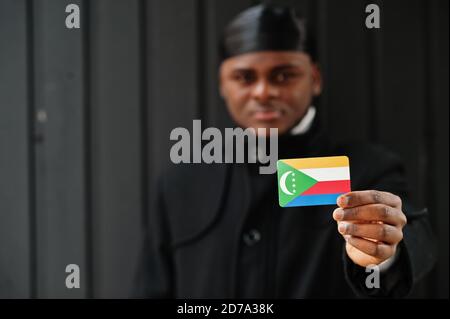 Afrikanischer Mann tragen schwarz durag halten Komoren Flagge bei der Hand isoliert dunklen Hintergrund. Stockfoto