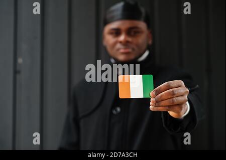 Afrikanischer Mann tragen schwarz durag halten Elfenbeinküste Flagge bei der Hand isoliert dunklen Hintergrund. Stockfoto