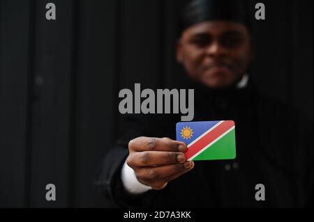 Afrikanischer Mann tragen schwarze durag halten Namibia Flagge bei der Hand isoliert dunklen Hintergrund. Stockfoto