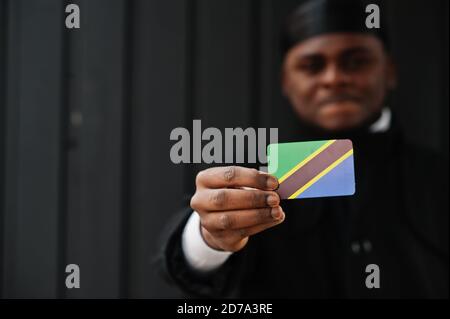 Afrikanischer Mann tragen schwarz durag halten Tansania Flagge bei der Hand isoliert dunklen Hintergrund. Stockfoto
