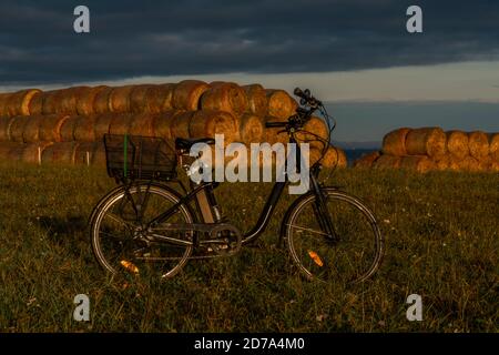 Heubälle und Elektrofahrrad auf dem Feld bei Ceske Budejovice Stadt in Sonnenaufgang Zeit in Farbe Herbst Stockfoto