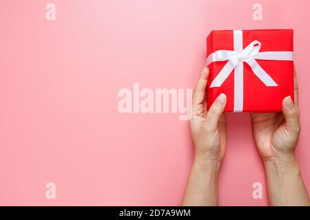 Flach Lay von Frau Hände halten Geschenk verpackt und mit Schleife isoliert auf rosa Hintergrund mit Kopie Raum dekoriert. Liebe zum Valentinstag. Geburtstagsmotiv. Stockfoto
