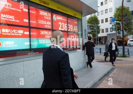 Ein Mann, der ein elektronisches Börsenboard mit steigenden Zinssätzen von Echtzeit-Trades in Tokio betrachtet. Stockfoto