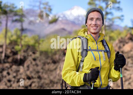 Wanderer Mann Wandern im Wald Berg Hintergrund. Glückliche gesunde junge fit Sportperson mit Rucksack, Jacke und Hut Trekking in der Natur im Frühjahr Stockfoto
