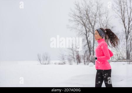 Winter Running Frau bei kaltem Schnee joggen draußen in winddichter Kleidung mit Handschuhen, Stirnband, Winterstrumpfhose und Windjacke in weiß Stockfoto