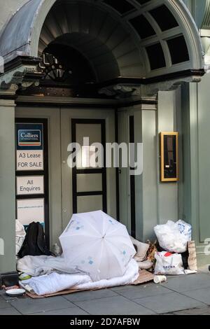 Mann, der in der Tür eines leeren Geschäftsgebäudes schlecht schläft Ein Microsoft Regenschirm leeren MacDonald Container und verschiedene Plastiktüten Stockfoto