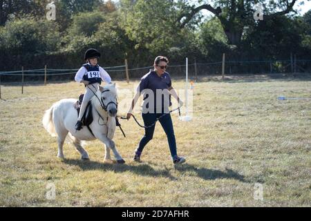 Frau führt kleine graue Pony und entschlossen jungen Reiter Beim lokalen Reiten gymkhana Wettbewerb England Stockfoto