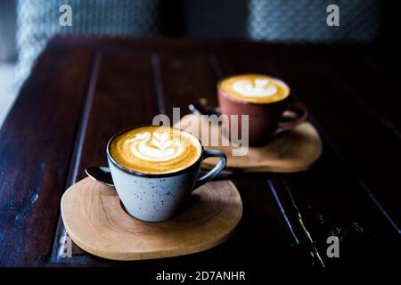 Zwei Tassen heißen Cappuccino auf Holztisch mit Löffeln auf dunklem Tischhintergrund. Frühstückszeit. Stockfoto