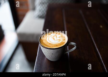 Graue Tasse heißen Cappuccino auf dunklem Holzschreibtisch Hintergrund. Frühstückszeit. Stockfoto