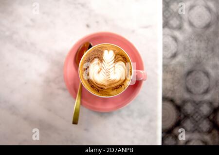 Rosafarbene Tasse heißen Cappuccino mit Latte-Kunst auf weißem Marmortisch. Frühstückszeit. Stockfoto