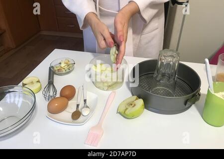 Die Frau schneidet Äpfel. Zimt und Backpulver in Teelöffel. Auf dem Tisch stehen Zutaten und Werkzeuge für die Herstellung von charlotte. Herbstkuchen mit App Stockfoto