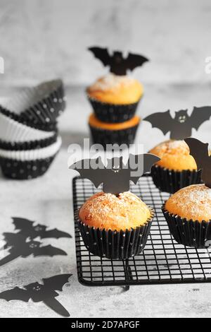 Halloween Kürbis Muffins in schwarzen Kapseln mit Karton Fledermäuse verziert. Festliche Halloween Cupcakes. Nahaufnahme des köstlichen gruseligen halloween Muf Stockfoto