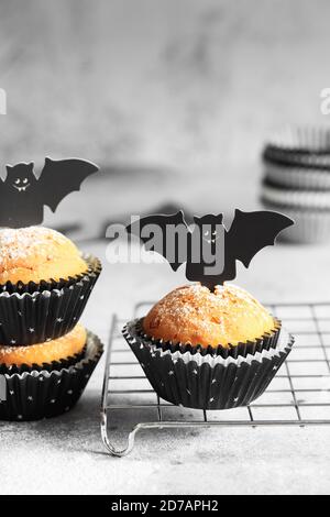 Halloween Kürbis Muffins in schwarzen Kapseln mit Karton Fledermäuse verziert. Festliche Halloween Cupcakes. Nahaufnahme des köstlichen gruseligen halloween Muf Stockfoto