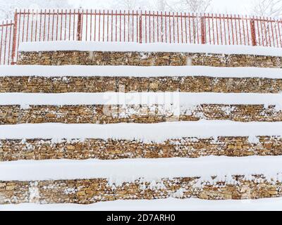Stufenwand aus Steinen mit einem Gitter mit befestigt Ein Zaun an der Spitze mit Schnee bedeckt Stockfoto