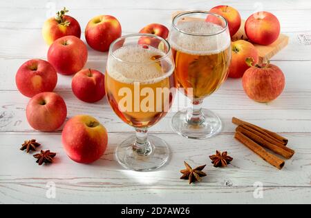Reife frische saftige rote Äpfel, Gewürze und Gläser mit Apfelwein auf einer hellen Holzoberfläche. Horizontale Ausrichtung, selektiver Fokus. Stockfoto