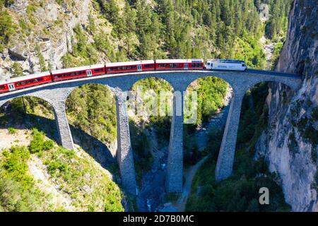 Atemberaubender Blick aus der Vogelperspektive auf den Zug vorbei am Landwasserviadukt in der Nähe von Filisur, roter Zug des Bernina Express, Schweiz Stockfoto