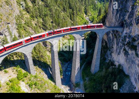 Atemberaubender Blick aus der Vogelperspektive auf den Zug vorbei am Landwasserviadukt in der Nähe von Filisur, roter Zug des Bernina Express, Schweiz Stockfoto